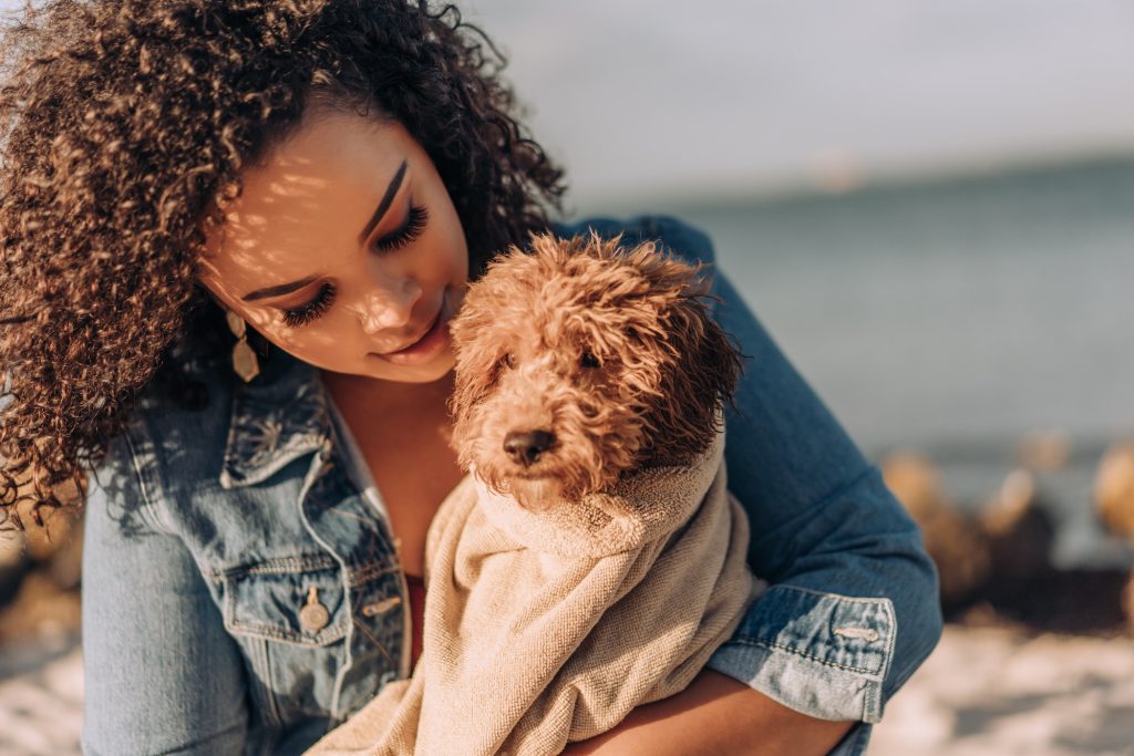 People and pets - woman with curly hair holding puppy dog wrapped in towel at the beach